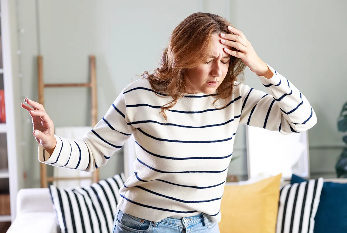 a woman at home holding a hand to her head due to dizziness
