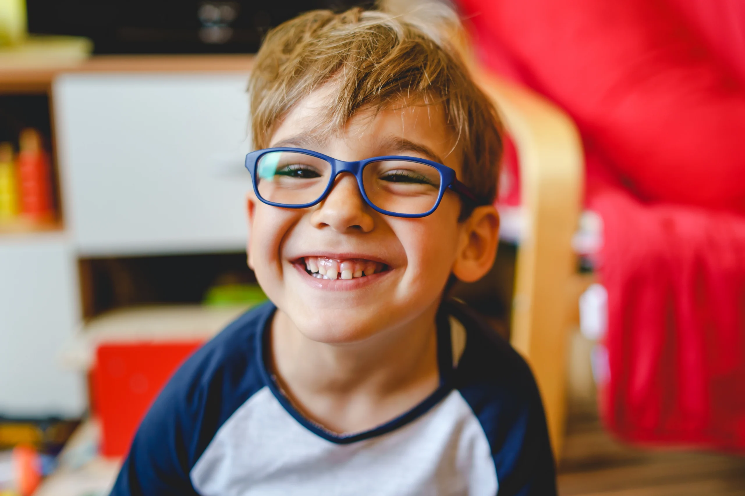 A grinning boy wearing a t shirt and blue framed glasses.