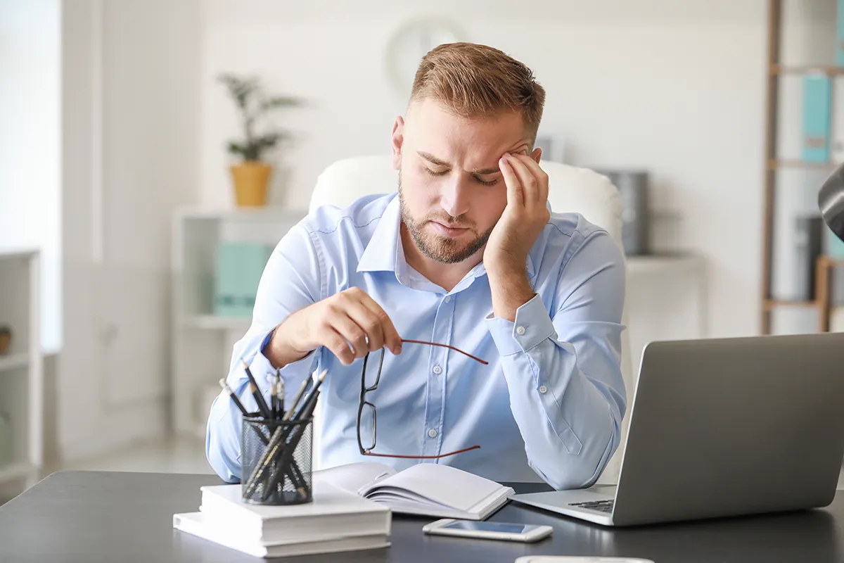 a man working on his computer and holding a hand to his head due to a headache