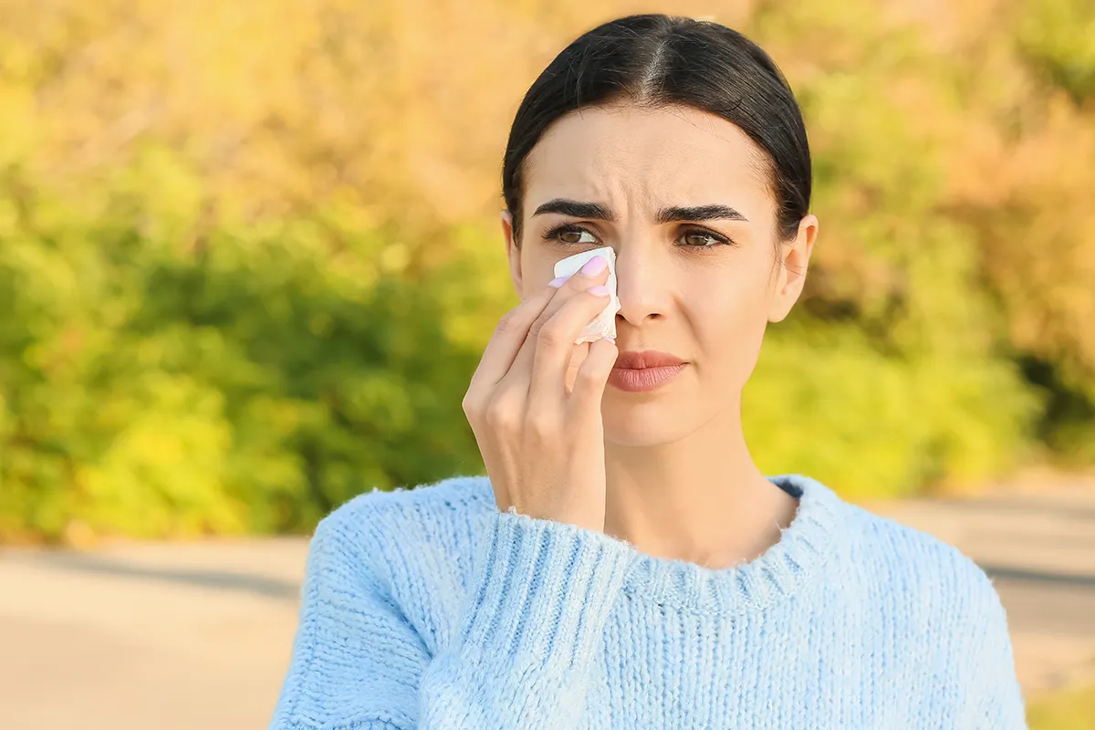 a woman standing outside looking uncomfortable and wiping her eye with a tissue