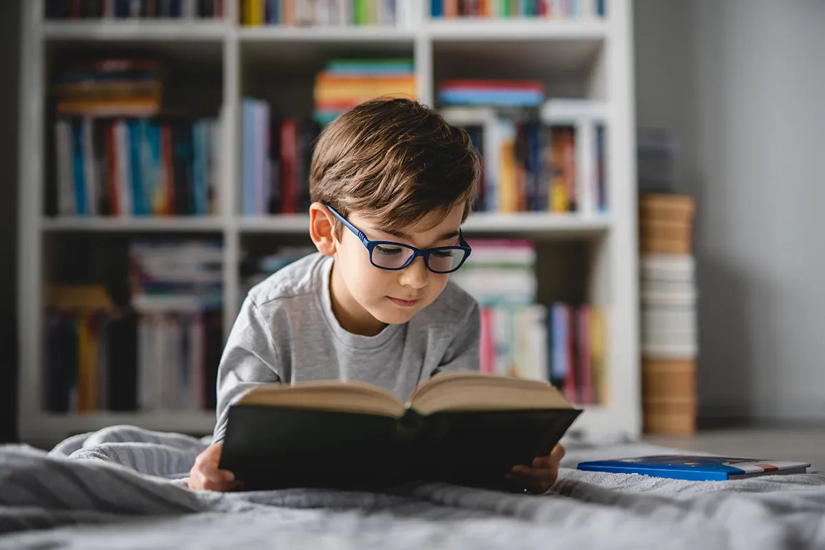 a little boy wearing glasses and reading a book
