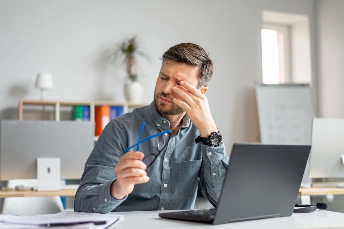 Man feeling pain eye strain, rubbing dry irritated eyes, fatigued from computer work, sitting in office